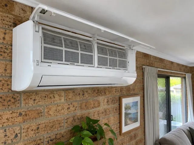 Clean split system with open front panel and visible filters on a brick wall in a living room in Robina
