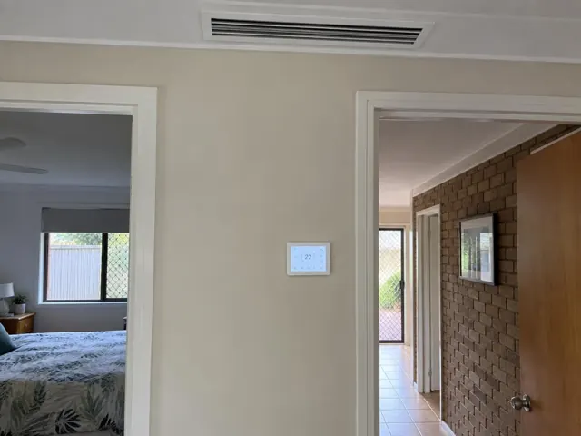 Ceiling ducted outlet and wall controller in a beige hallway with adjoining rooms in Burleigh Waters