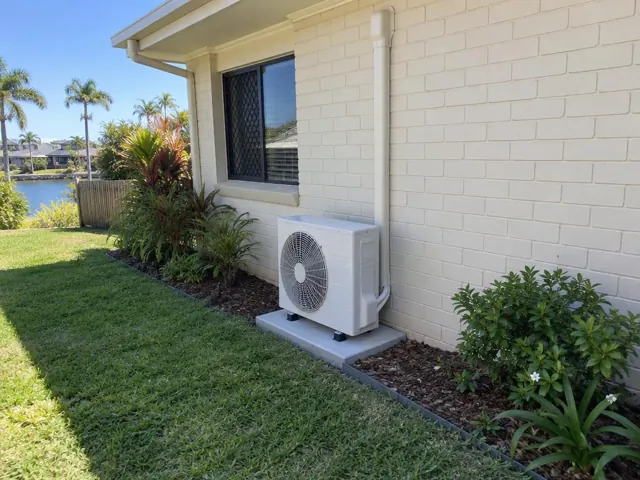 Outdoor air conditioner condenser on a concrete pad beside a cream brick house in Burleigh Waters