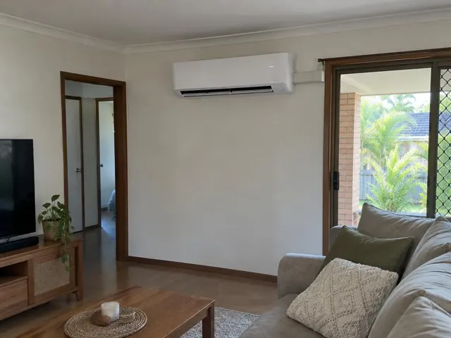 Living room with a wall-mounted split system above timber trim and a sliding door in Varsity Lakes